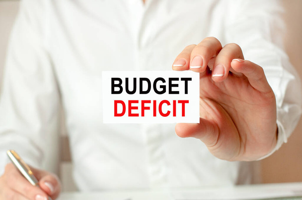 женщина в белой рубашке держит лист бумаги с текстом: дефицит бюджета. бизнес-концепция для компаний. - Фото, изображение