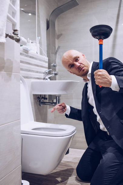 Un uomo che tiene uno stantuffo per pulire un water tappato. - Foto, immagini