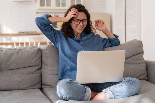 Mutlu kadın kanepeye oturur heyecandan başını yolar dizüstü bilgisayar ekranında haberleri okur, neşeli bir gülümsemeyle. - Fotoğraf, Görsel
