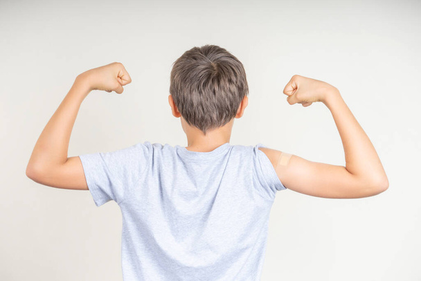 Tienerjongen met pleister op zijn arm maakt vuist en buigt haar biceps na vaccinatie. Injectie covid vaccin, gezondheidszorg voor kinderen - Foto, afbeelding