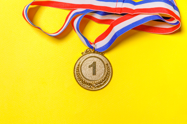 Jednoduše plochý ležel vítěz designu nebo mistr zlatá trofej medaile izolované na žlutém barevném pozadí. Vítězství je první místo v soutěži. Vítězství nebo úspěch. Prostor pro kopírování horního pohledu - Fotografie, Obrázek