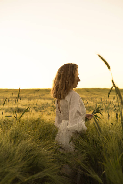 young beautiful woman with blond long hair in a white dress on a wheat field. Flying hair in the sun, summer. Time for dreamers, golden sunset. - Photo, image
