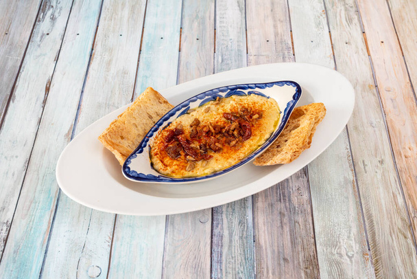 Фарфоровая тарелка с куриным хумусом, семенами подсолнечника и обезвоженными помидорами и паприкой сверху в сопровождении нескольких кусочков хлеба для окунания - Фото, изображение