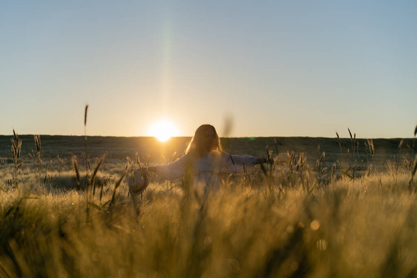 young beautiful woman with long blond hair in a white dress on a wheat field in the early morning at sunrise. Summer is the time for dreamers, flying hair, a woman running across the field in the rays of the sun. travels - Zdjęcie, obraz