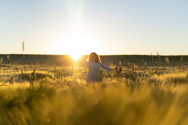 young beautiful woman with long blond hair in a white dress on a wheat field in the early morning at sunrise. Summer is the time for dreamers, flying hair, a woman running across the field in the rays of the sun. travels - Zdjęcie, obraz