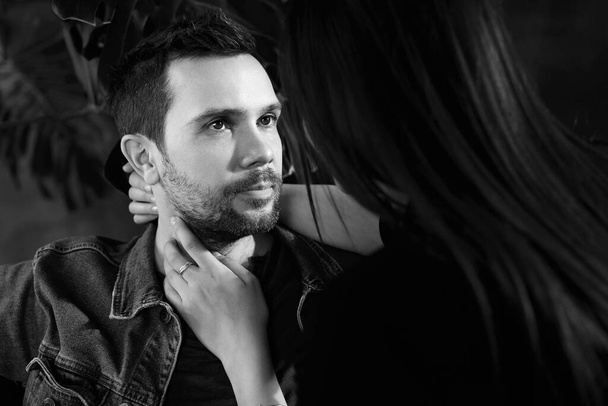 Black and white portrait of a man hugged by a woman. An unshaven handsome man of about thirty looks at his beloved woman - Photo, Image