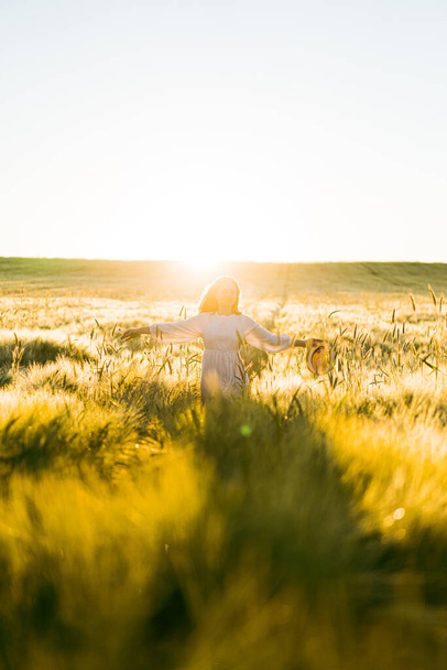 young beautiful woman with long blond hair in a white dress on a wheat field in the early morning at sunrise. Summer is the time for dreamers, flying hair, a woman running across the field in the rays of the sun. travels - Foto, afbeelding