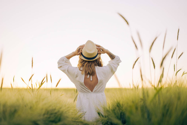 young beautiful woman with blond long hair in a white dress in a straw hat on a wheat field. Flying hair in the sun, summer. Time for dreamers, golden sunset. - Zdjęcie, obraz