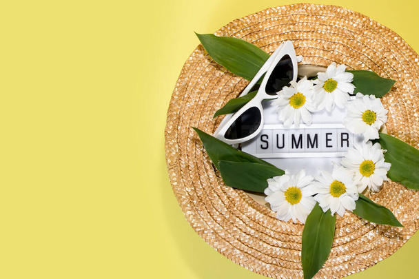 Womens summer straw hat on yellow background top view flat lay copy space. Summer travel vacation concept, single item. Text SUMMER from letters and field chamomiles flowers on yellow background. - Photo, Image