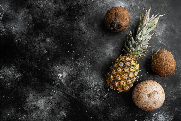 Frutas exóticas frescas, conjunto de abacaxi e coco, em fundo de mesa de pedra escura preta, vista superior plana, com espaço de cópia para texto - Foto, Imagem