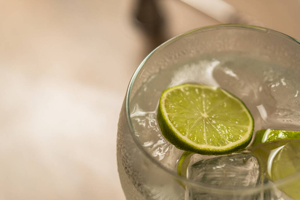 Close-up of a gin and tonic cocktail with a slice of lemon against the light. - Фото, изображение