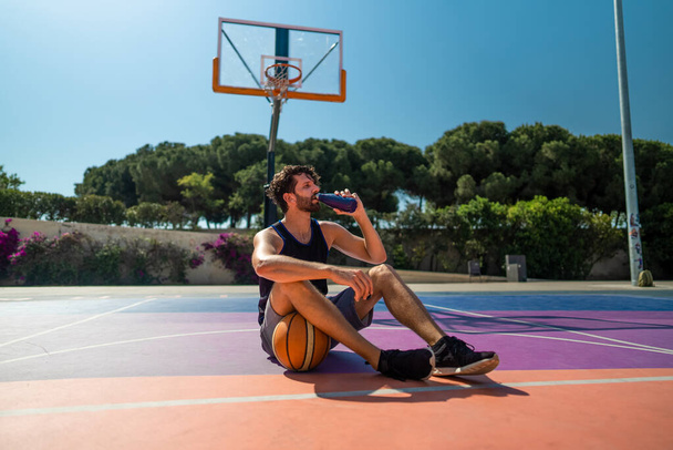 Уставший баскетболист пьет воду после тренировки. пополнение водного баланса - Фото, изображение