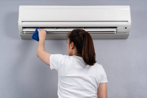 young woman cleaning the air conditioner with cloth at home - Foto, Bild