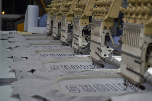 Reihe großer Nähmaschinen in einer industriellen Nähfabrik, die an grauen Jacken arbeitet - Foto, Bild