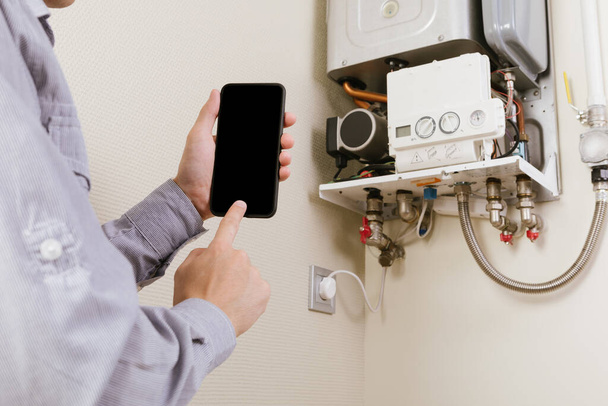 online diagnostics of household appliances via a mobile phone. a man repairing a boiler - Foto, immagini