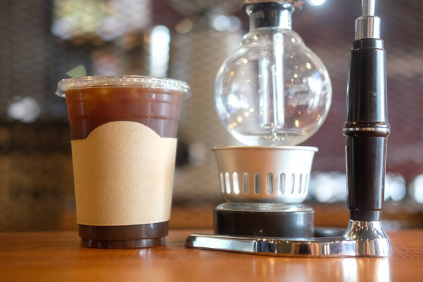 Lähikuva lasi jäätä mustaa kahvia ja kahvia panimo vempaimia puinen baari laskuri. - Valokuva, kuva