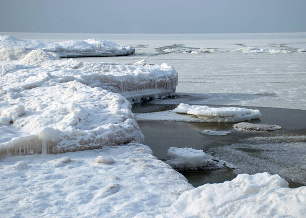 χειμερινό τοπίο δίπλα στη θάλασσα, χιονισμένα, ενδιαφέροντα σχήματα πάγου στην ακτή της θάλασσας, αμμόλοφοι καλυμμένοι με ένα λευκό στρώμα λαμπερό χιόνι, χειμώνας - Φωτογραφία, εικόνα