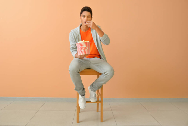African-American teenager eating popcorn near color wall - Foto, imagen