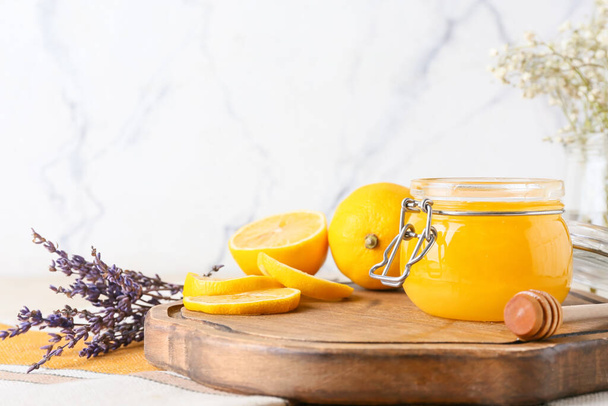 Tablero con tarro de miel, limones y flores sobre fondo claro, primer plano - Foto, Imagen
