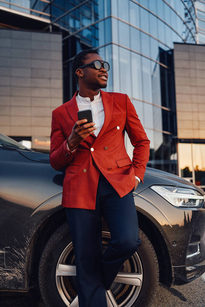 Cheerful african businessperson with phone and car outside - Foto, immagini