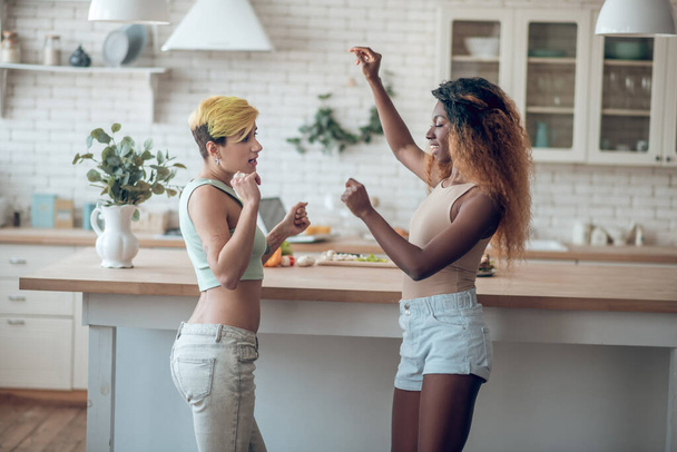Two girlfriends dancing in kitchen during day - Foto, immagini