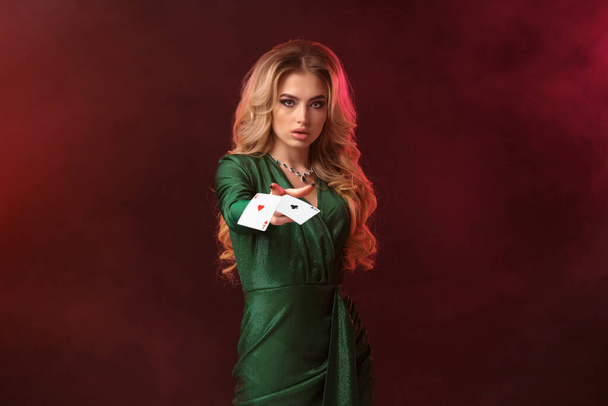Blonde lady, make-up, in green dress and jewelry. Holding something or throwing it, posing on colorful smoky background. Copy space, close up - Foto, Bild