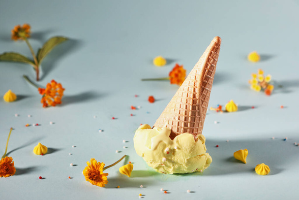 Lemon ice cream with waffle cone on blue background with yellow flowers - Photo, Image