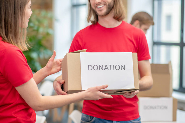 Guy holding out packed donation box to girl - Foto, Bild