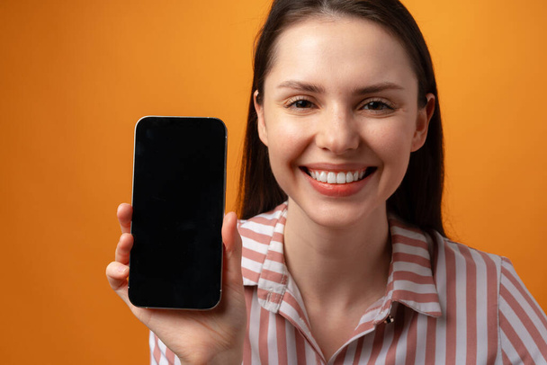 Happy smiling young woman showing you black smartphone screen with copy space - Foto, immagini