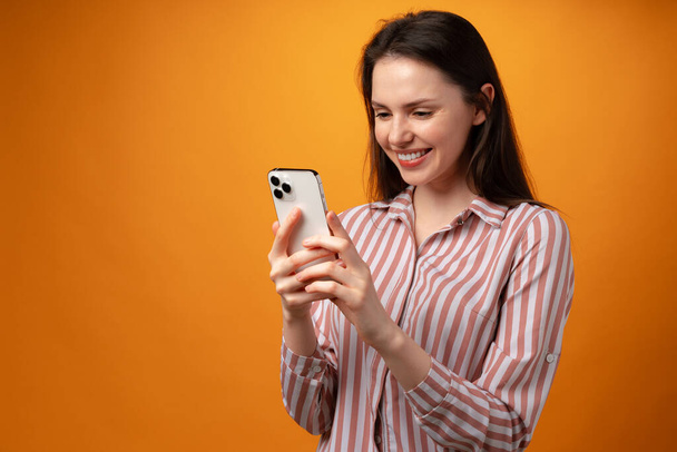 Portrait of young attractive woman using her smartphone against yellow background - Fotó, kép
