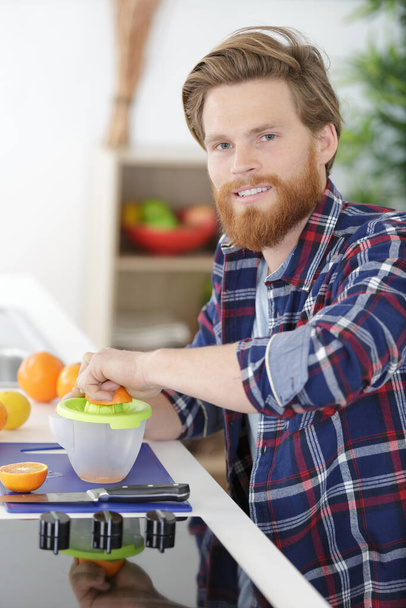 happy healthy handsome man making organic orange fruit juice - Photo, image