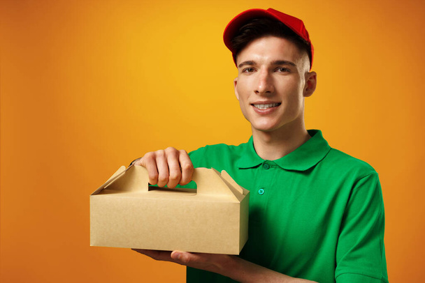 Delivery person holding parcel with food delivery against yellow background - 写真・画像