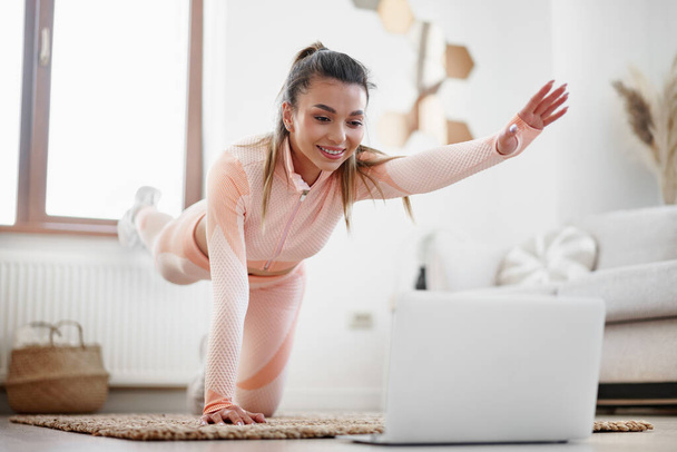 Spor giyim sektöründe genç bir kadın evde egzersiz videoları izlemek için dizüstü bilgisayar kullanıyor. - Fotoğraf, Görsel