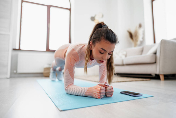 Urheileva nuori nainen tekee lankku liikuntaa sisätiloissa kotona - Valokuva, kuva