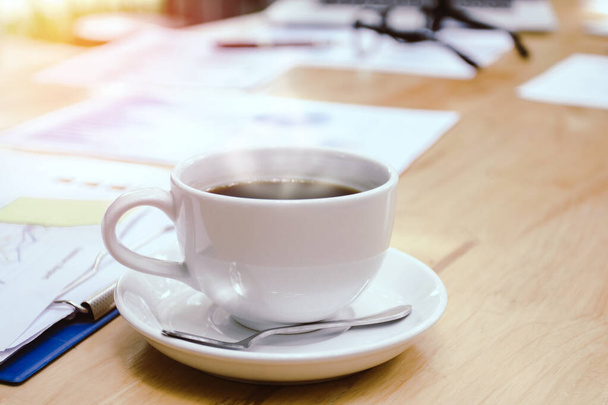 Tasse weißen Kaffee mit Rauch vorhanden. Ordner und Dokumente auf dem Schreibtisch mit Brille und Laptop - Foto, Bild