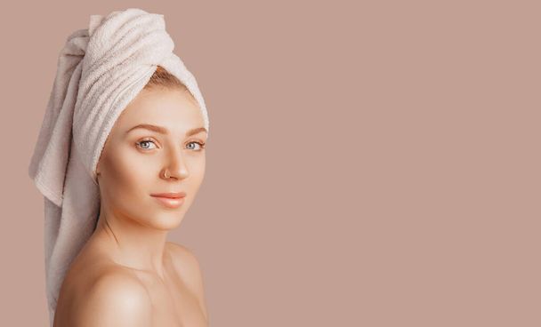 Beautiful sensual young girl with clean skin on a beige background with a mockup. Topless woman in a towel. The concept of spa treatments, natural beauty and care, youth, cream and mask, freshness - Valokuva, kuva
