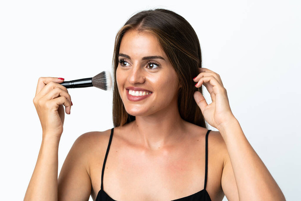 Jonge Uruguayaanse vrouw geïsoleerd op witte achtergrond met make-up borstel - Foto, afbeelding