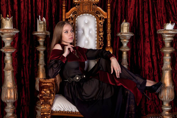 Medieval queen in historical attire on golden throne in castle. Portrait of young woman in an old style dress on an antique throne in reception room of fortress. Concept of themed costume events - Fotoğraf, Görsel