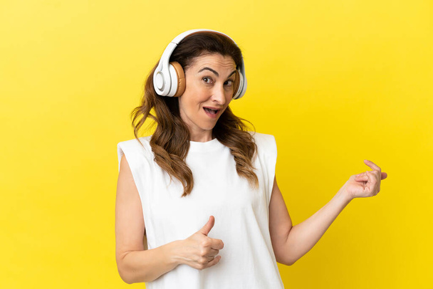 Middle aged caucasian woman isolated on yellow background listening music and doing guitar gesture - Foto, immagini