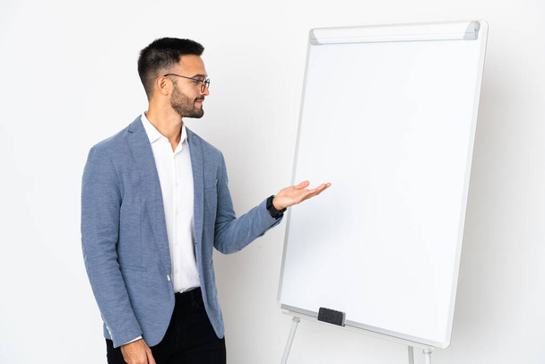 Young caucasian man isolated on white background giving a presentation on white board - Fotó, kép