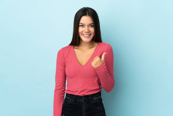 Adolescente isolée sur fond bleu pointant vers le côté pour présenter un produit - Photo, image