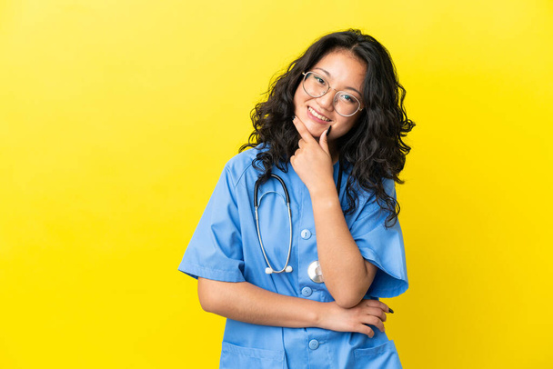 Mladý chirurg lékař asijské žena izolovaný na žlutém pozadí s úsměvem - Fotografie, Obrázek