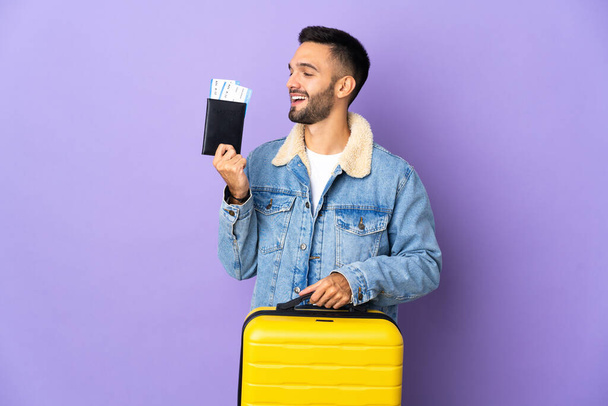 Молодой кавказский мужчина на голубом фоне в отпуске с чемоданом и паспортом - Фото, изображение