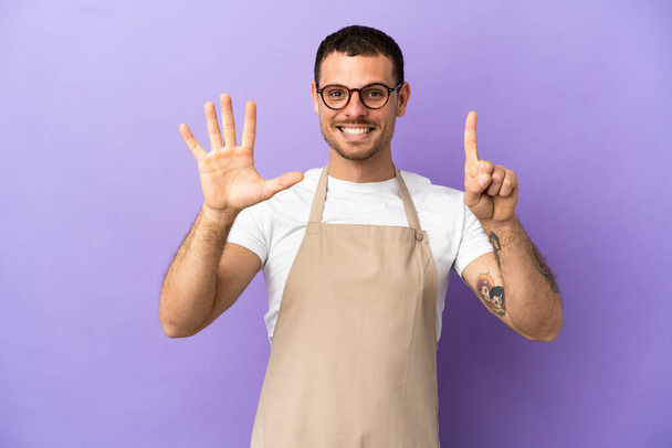 Serveur restaurant brésilien sur fond violet isolé comptant six avec les doigts - Photo, image