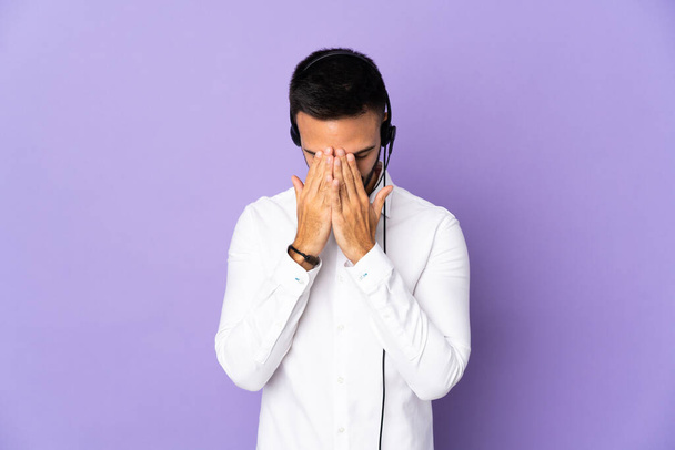 Hombre telemarketer trabajando con un auricular aislado sobre fondo púrpura con expresión cansada y enferma - Foto, Imagen