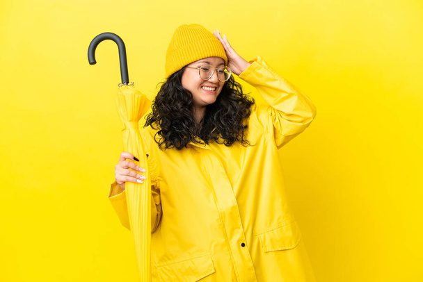 Asiatico donna con impermeabile e ombrello isolato su sfondo giallo sorridente molto - Foto, immagini