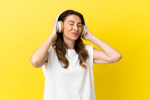 Mulher caucasiana de meia idade isolada em fundo amarelo ouvindo música e cantando - Foto, Imagem