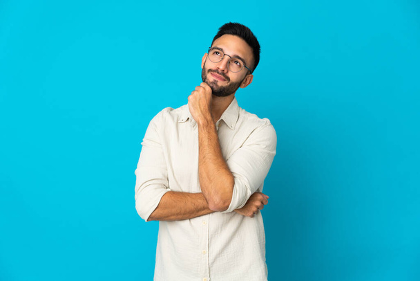 Young caucasian man isolated on blue background and looking up - Photo, Image