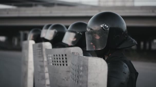 Plan moyen de policiers anti-émeute vêtus d'équipement complet et tenant des boucliers debout dans la rangée L'un d'eux se retournant et regardant la caméra - Séquence, vidéo