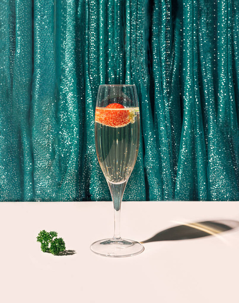 A glass of champagne cocktail with some parsley on the bottom in front of green glossy curtain. Theatre sparkle modern concept. - Photo, Image